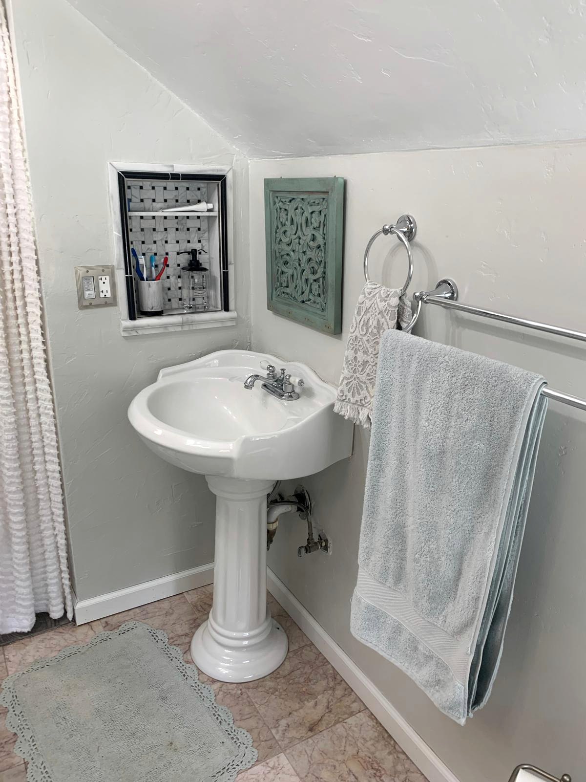 White pedestal sink and inset marble mosaic storage niche beneath the attic eaves