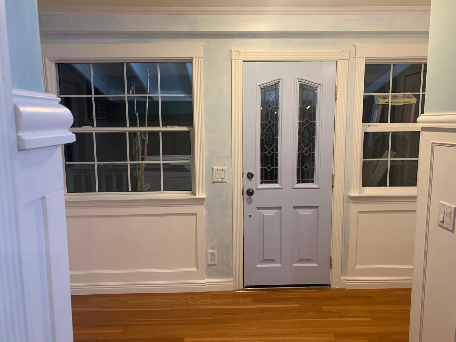 Finished 1952 California farmhouse entry showing white paneled walls, trimmed windows, front door, and warm wood floor