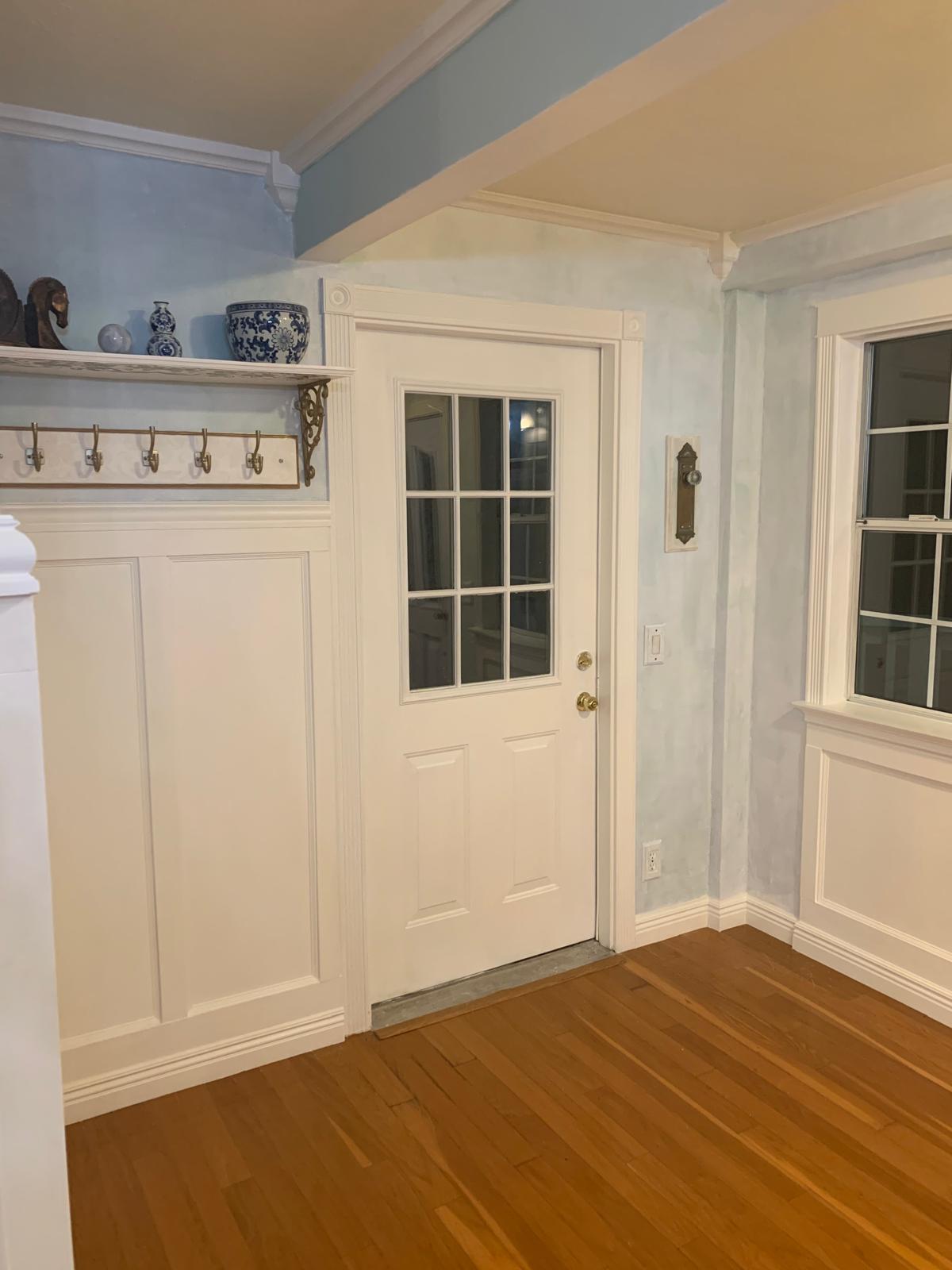 Finished California farmhouse entry with white wall paneling, soft blue walls, substantial door trim, and warm wood floors