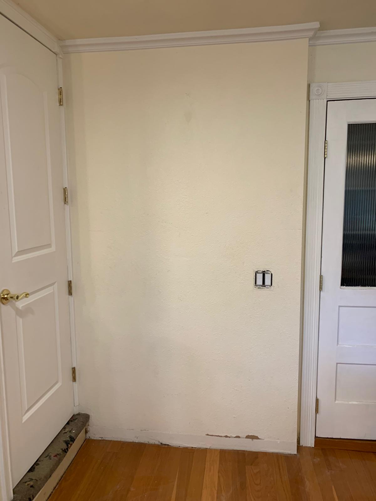 Before photograph of a plain farmhouse entry wall beside the pantry opening