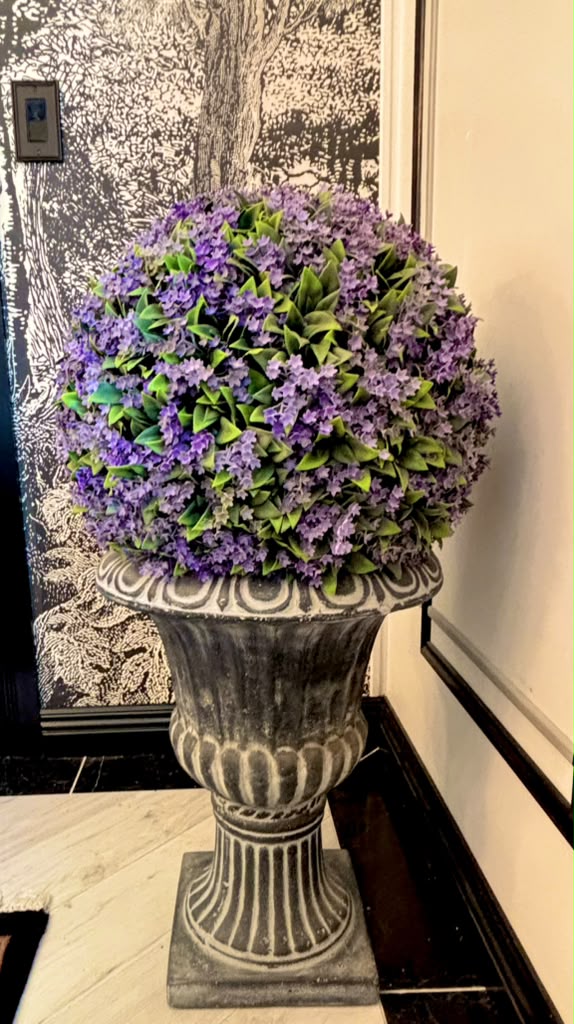 Purple flowers arranged in a classical urn beside the scenic mural and black architectural trim