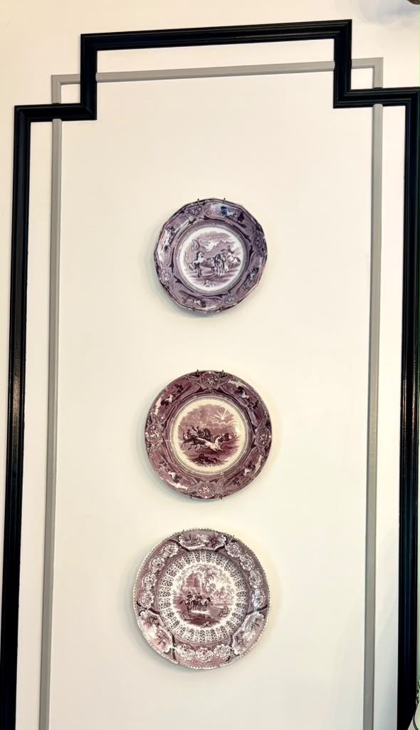 Crossing black and tonal-gray millwork framing three antique equestrian transferware plates